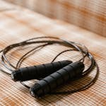 Close-up of a black jump rope resting on a brown plaid surface indoors.